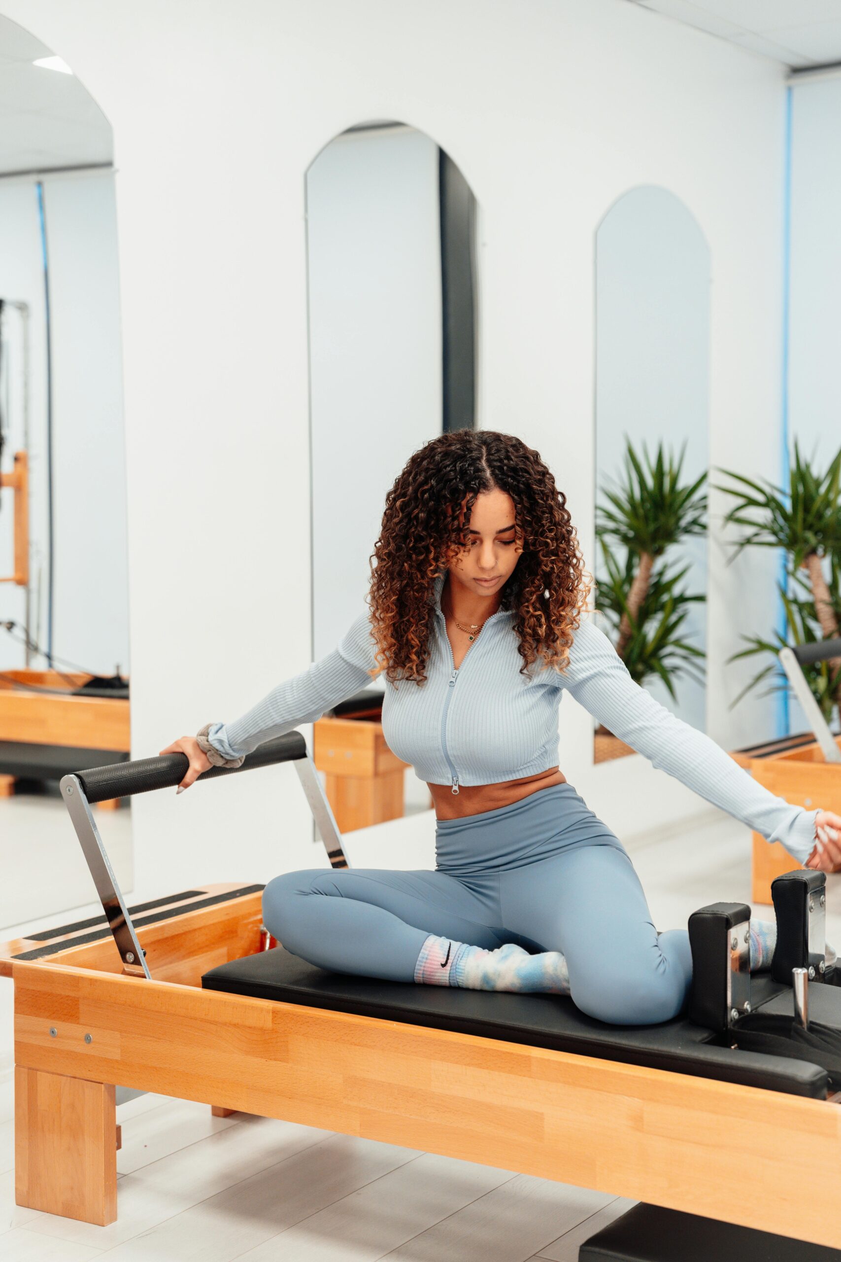 Woman performing pilates on a reformer machine indoors, promoting fitness and well-being.