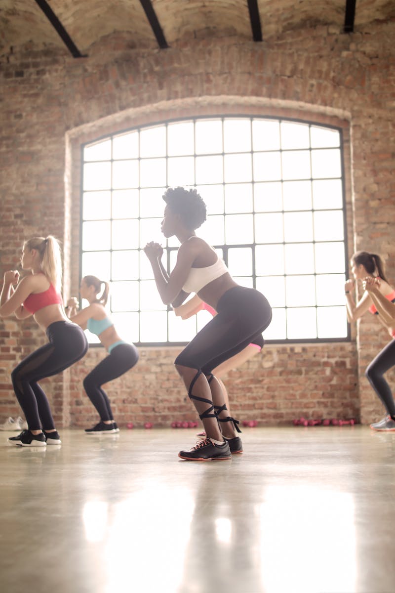 Women participating in a group fitness class performing squats in an industrial-style studio.
